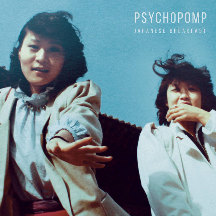 Cover for the album Psychopomp by Japanese Breakfast. Two young Korean women in white coats look down at a camera on a windy day. The woman on the left, Chongmi, is reaching out toward the camera