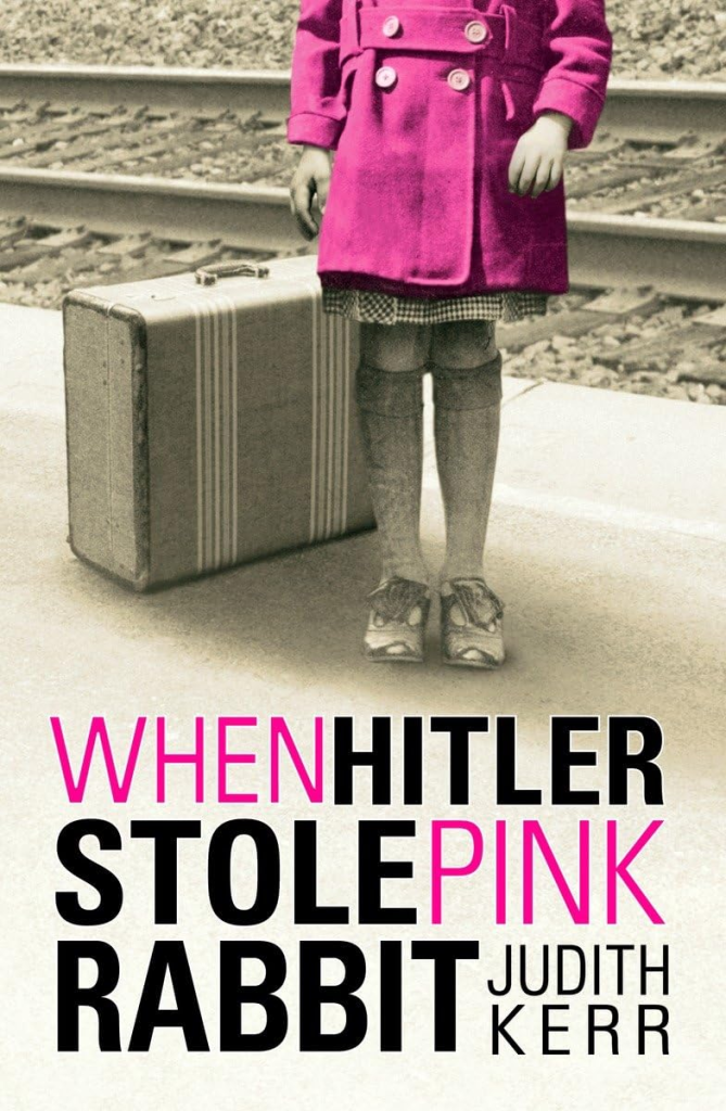 cover for When Hitler Stole Pink Rabbit by Judith Kerr. A young girl, shown from the chest down stands at a train track with a suitcase behind her. Her pink overcoat is the only color against the sepia background.